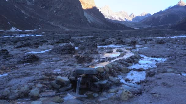 背後に山のある凍った草に囲まれたパイプに流れる運河の小さな流れ — ストック動画