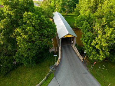 An aerial view of a covered bridge spanning a creek and surrounded by trees.