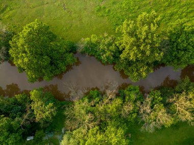 An aerial straight down view of a creek bordered by trees and fields.