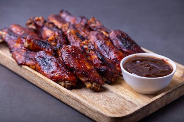 Ahşap bir tahtanın üzerinde ızgara soslu kızarmış tavuk kanadı. Siyah arkaplan, yakın plan.