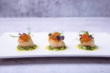 Havyarlı deniz tarakları, mikroyeşiller ve beyaz tabakta yeşil sos. Yakın plan..