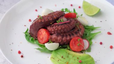 Ahtapot salatası, kiraz domatesleri, avokado, roka, bıldırcın yumurtası, turp ve beyaz tabakta limon. Geleneksel Akdeniz yemeği. Yakın plan, beyaz arkaplan, kamera kaldırma.