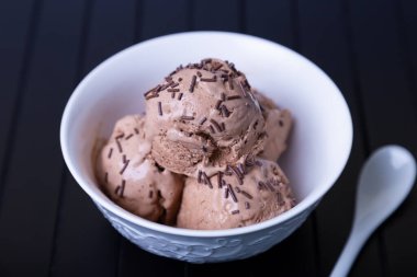 Siyah arka planda beyaz bir kaseye çikolata serpiştirilmiş çikolatalı dondurma. Üç top ev yapımı dondurma. Yakın plan..