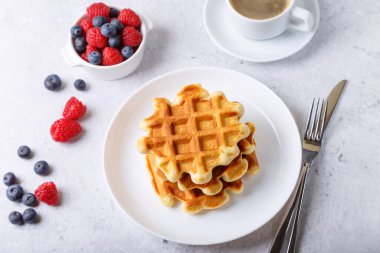 Beyaz bir tabak ve bir fincan kahve üzerinde taze böğürtlen (ahududu ve yabanmersini) ile Viyana ya da Belçika waffleları. Geleneksel tatlı. Yakın plan, beyaz arkaplan, üst görünüm.