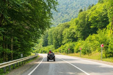 Kafkasya, Rusya - 10 Ağustos 2021: Kafkasklı bir çift, dağ zirveleri arka planında Kafkasya dağlarında ATV kullanıyor. Dörtlü bisiklet macerası ve doğa keşfi konsepti