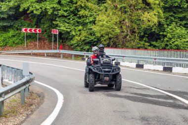 Arkhyz, Rusya - 10 Ağustos 2021: Kafkaslı bir çift, dağ zirveleri arka planında Kafkasya dağlarında ATV kullanıyor. Dörtlü bisiklet macerası ve doğa keşfi konsepti