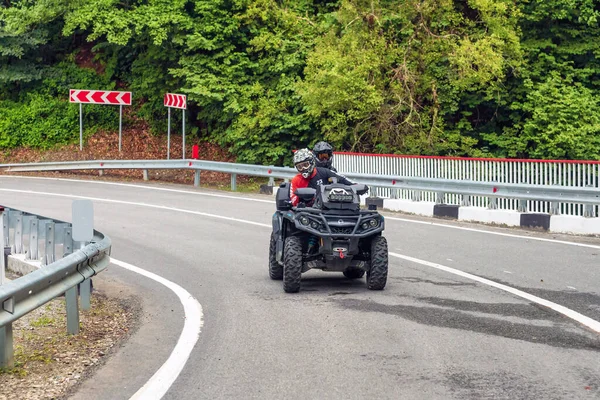 Arkhyz, Rusya - 10 Ağustos 2021: Kafkaslı bir çift, dağ zirveleri arka planında Kafkasya dağlarında ATV kullanıyor. Dörtlü bisiklet macerası ve doğa keşfi konsepti