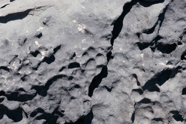 Koyu gri kayaların yüzey yüzeyini çatlatmış. Dağın bir parçası dışarıda. Gölgeleri ve güneş ışığıyla kusursuz doğal bir zemin. Esmer taş arka plan. Dağ dokusu. Yakın çekim.. 