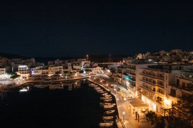 Yunanistan 'ın Girit adasındaki küçük bir kasaba olan Agios Nikolaos ve Voulismeni gölünün güzel gece manzarası. Sahilde kafe, restoran, tekne ve dağları olan bir yer.