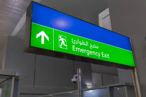 Emergency exit sign in English and Arabic glowing green at airport