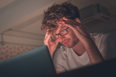 Gözlüklü bir erkek evde dizüstü bilgisayarın önünde çalışıyor..