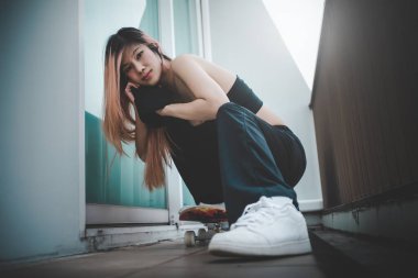 Asyalı manken kız sokak modası için beyaz spor ayakkabıları ve kaykayla poz veriyor.