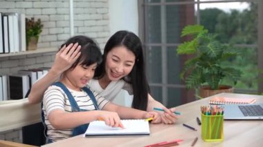 Asyalı anne, ev okulunda ve çevrimiçi derslerde kızına boyama kitabı ödevinde yardım ediyor. 