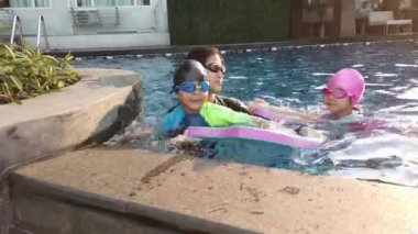 Asyalı Anne Öğretmen, küçük çocuklara mutluluk ve neşe içinde birlikte yüzme dersi veriyor..