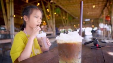 Asyalı bir kız kafede oturmuş, çikolatalı buzlu içecek ve ahşap masada kahve içiyor..