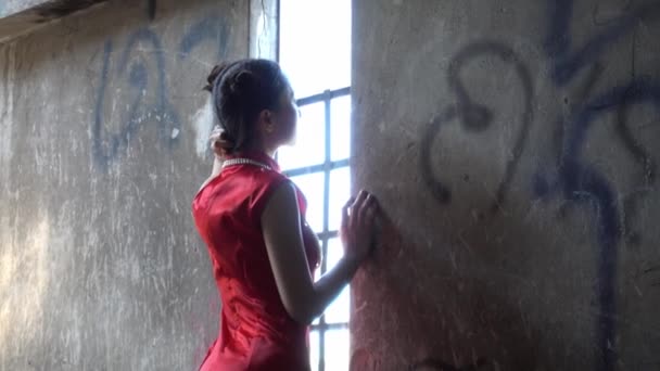 中国女孩穿着中国传统的红色长袍 站在一座乡村建筑的窗前 站在灯光下 — 图库视频影像