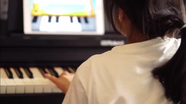 アジアの女性はタブレット上でオンライン音楽レッスンでピアノを練習しています バックビュー — ストック動画