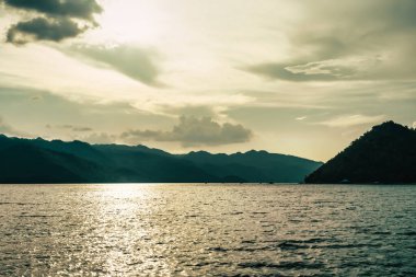 silhouette Island mountain in open water with golden sunset sky reflection.