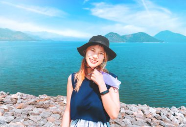 Şapkalı ve yaz kıyafetli Asyalı kadın sahilde tatil yaparken resim çekiyor..