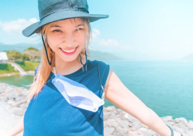 Şapkalı ve yaz kıyafetli Asyalı kadın sahilde tatil yaparken resim çekiyor..