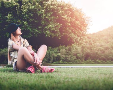 Kadın parkta büyük bir ağacın yanında oturuyor, doğa ve özgürlük kavramı için...