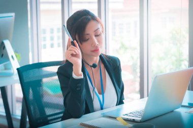 Asyalı kadın operatör, tele pazarlama bürosundaki servis müşterisiyle telefonda konuşuyor..