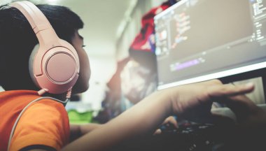 Asyalı çocuk, bilgisayar başında kulaklığı açık bir şekilde oyun programında kod yazma ve betik yazıyor..