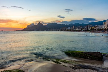 Ipanema sahilindeki Rio de Janeiro şehrinin dağlarının ardında güzel bir günbatımı.