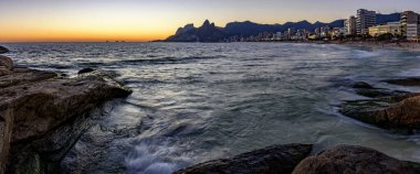Rio de Janeiro 'daki Ipanema plajında gün batımının panoramik görüntüsü. Şehrin karakteristik binaları ve dağları..