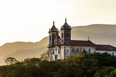 Ouro Preto 'daki eski kilise tepenin üstünde ve gün batımında tepelerle çevrili.