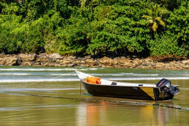 Brezilya 'nın Sao Paulo eyaletinde Bertioga' da güneşli bir günde arka planda kayalar ve yağmur ormanlarıyla kumsalda duran sürat teknesi.