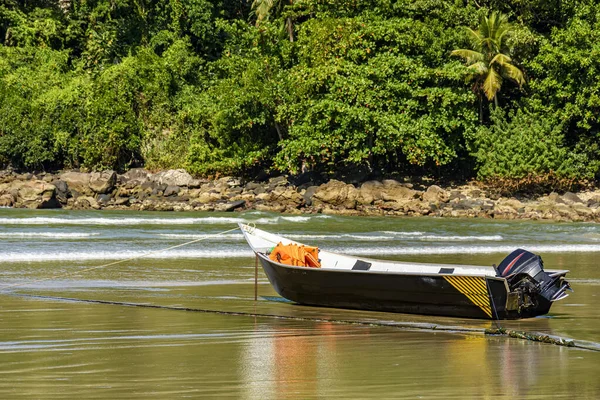 Brezilya 'nın Sao Paulo eyaletinde Bertioga' da güneşli bir günde arka planda kayalar ve yağmur ormanlarıyla kumsalda duran sürat teknesi.
