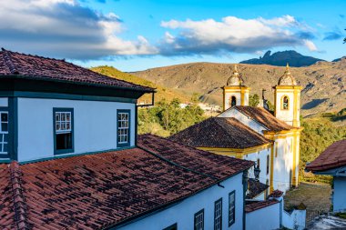 Barok mimarisinde tarihi kilise kulesi ve Ouro Preto, Minas Gerais 'in arka planında dağlar olan eski koloni evleri.