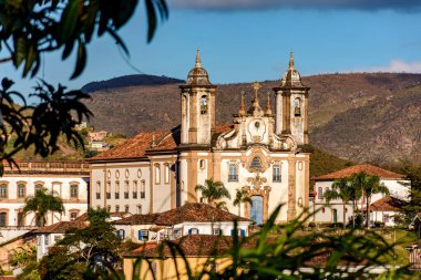 Ouro Preto şehrinin en büyük tarihi kiliselerinden biri arka planda dağlarla birlikte bitki örtüsünün içinden görülüyor.