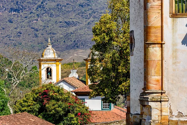 Facade and towers of a baroque church hidden among the vegetation with the hill in the background in the historic city of Ouro Preto in Minas Gerais, Brazil