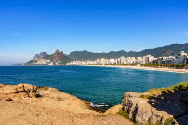 Rio de Janeiro 'daki Ipanema plajının manzarası. Deniz, binalar ve tepelerin olduğu güzel bir günde.