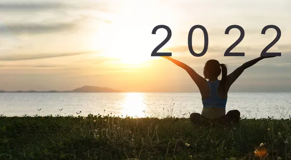 Mutlu yıllar 2022. Güzel bir gün batımı arka planına sahip çimenlerin üzerindeki bir kız silueti..