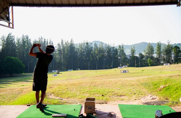 Asian golfer Man swing golf ball practice at golf driving range on evening on time for healthy sport. Lifestyle and Sport Concept