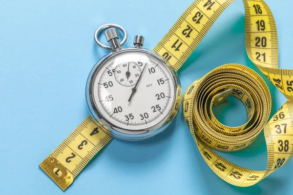 Gewichtsverlies trainingen. Gele meetlint meter en stopwatch op een blauwe achtergrond — Stockfoto