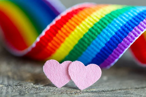 레즈비언 사랑의 상징으로 분홍색 하트 두 개가 있습니다. 성 소수자 커뮤니티 깃발 색깔의 무지개 리본 배경 — 스톡 사진