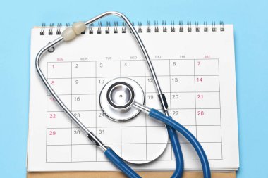 Takvim ve steteskop mavi arka planda. Bir doktor tarafından planlanmış muayene konsepti
