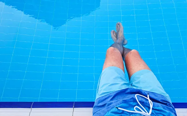 De man zit aan de rand van het zwembad met zijn voeten naar beneden in het water. Ontspan concept. Sjabloon Kopieer ruimte voor tekst — Stockfoto