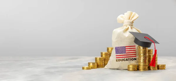 Oktatás az USA-ban. Drága oktatás. Egy halom érme egy pénzeszsákkal, amerikai zászlóval és diplomás sapkával. — Stock Fotó