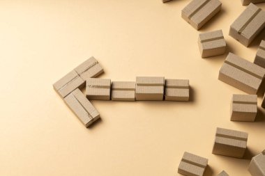 Açık kahverengi arka planda, karton kutulardan sola bakan ok.