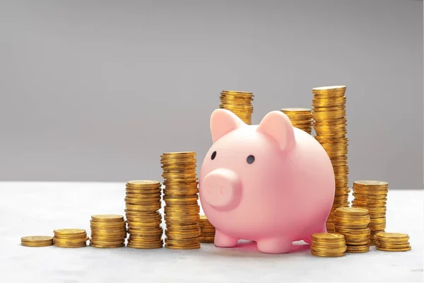 Piggy bank e uma pilha de moedas de ouro em um fundo cinza — Fotografia de Stock