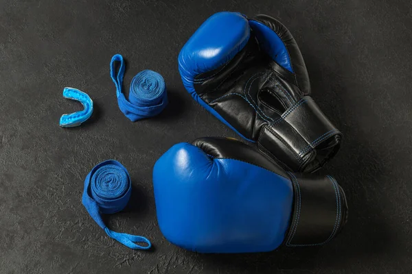 Blue boxing gloves with a cap and bandages on a black background.
