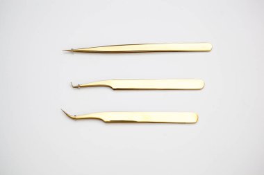 Kirpik uzatma ve kaş tasarımı için araçlar. Beyaz arka planda altın renkli kozmetik cımbızlar