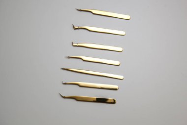 Kirpik uzatma ve kaş tasarımı için araçlar. Beyaz arka planda altın renkli kozmetik cımbızlar