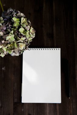 Siyah ahşap arka planda ortanca dalı olan beyaz bir defter aç