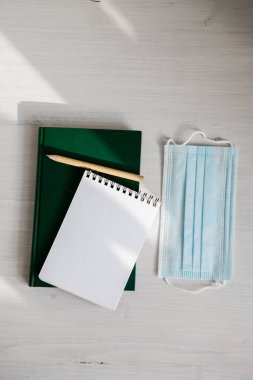 Yeşil bir günlükte açık beyaz bir defter, arka planda çevre dostu bir kalem, tıbbi bir maske ve yeşillik dalı.
